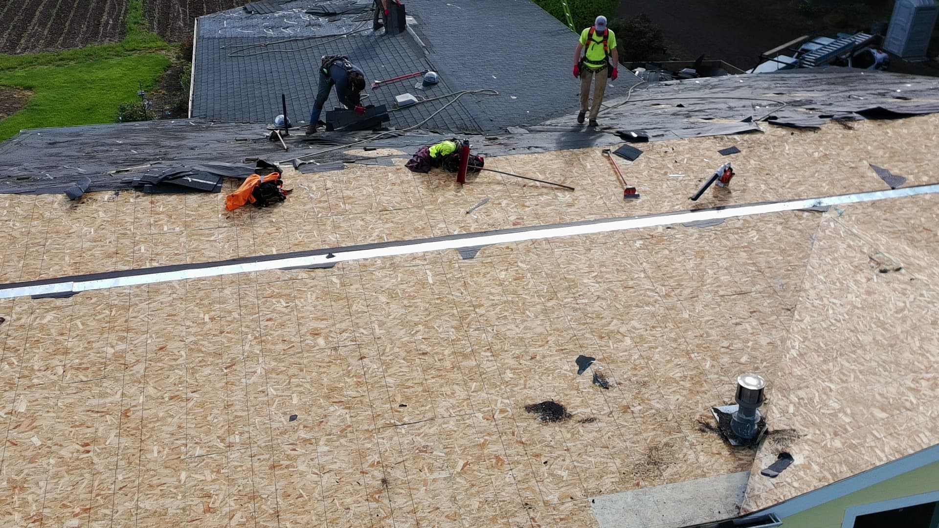 Roofers working on exposed roof decking after removing worn shingles from a home